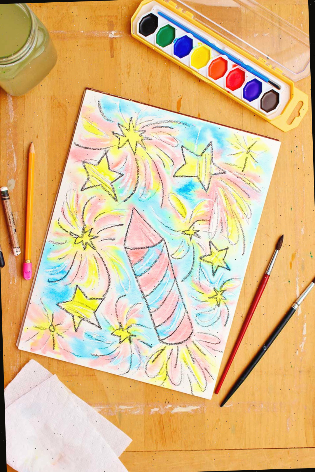 A resistência em aquarela completa repousa sobre uma mesa de madeira com aquarelas, um copo d'água, pincéis e toalhas de papel por perto.