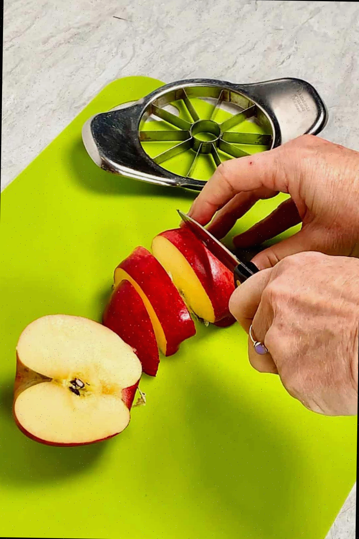 Pessoa fatiando maçãs com uma faca em uma tábua de corte verde brilhante.