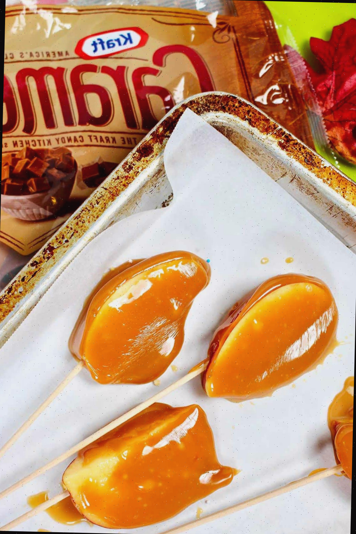 Fatias de maçã caramelizada dispostas sobre papel manteiga em cima de uma embalagem vazia de Kraft Caramel Bites.