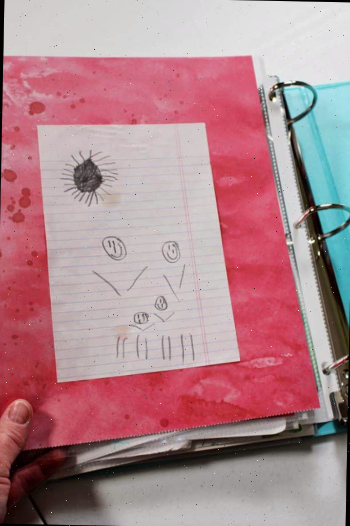 Desenho a lápis de uma criança de uma família e um sol em uma página de um fichário.