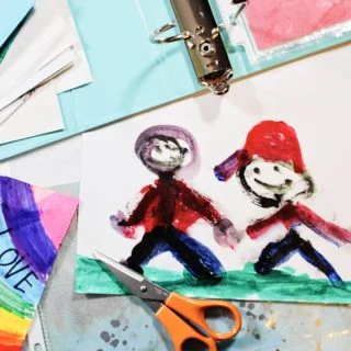 Pintura de uma criança de duas pessoas de mãos dadas, com tesouras, um fichário e papel de scrapbook nas proximidades.
