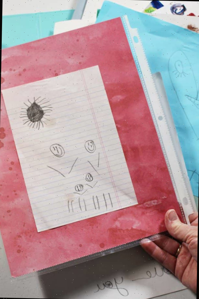 Desenho a lápis de uma criança de uma família e sol, montado em papel de scrapbook e dentro de um protetor de folha.