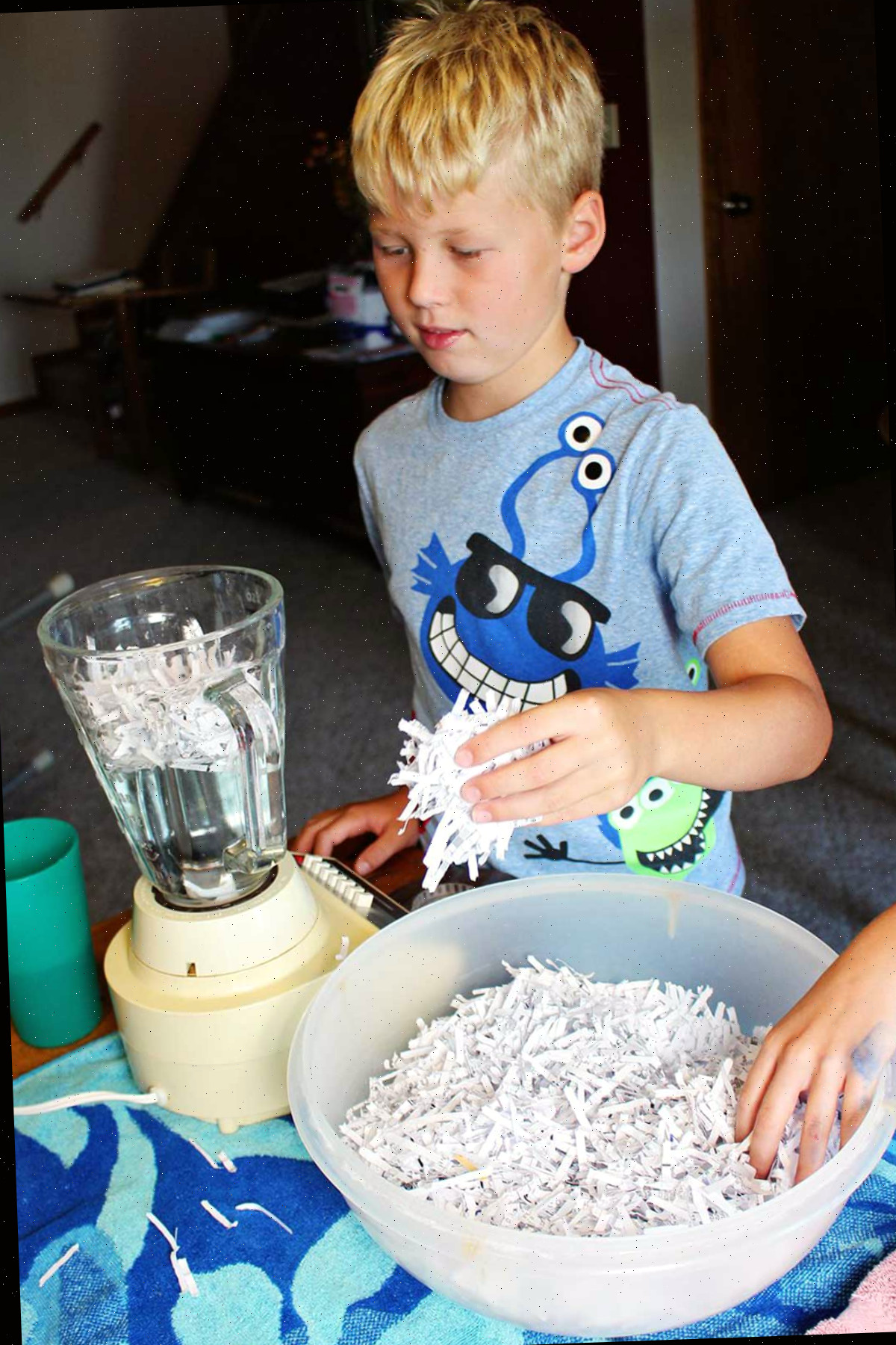 Uma criança adicionando papel picado a um liquidificador com água.