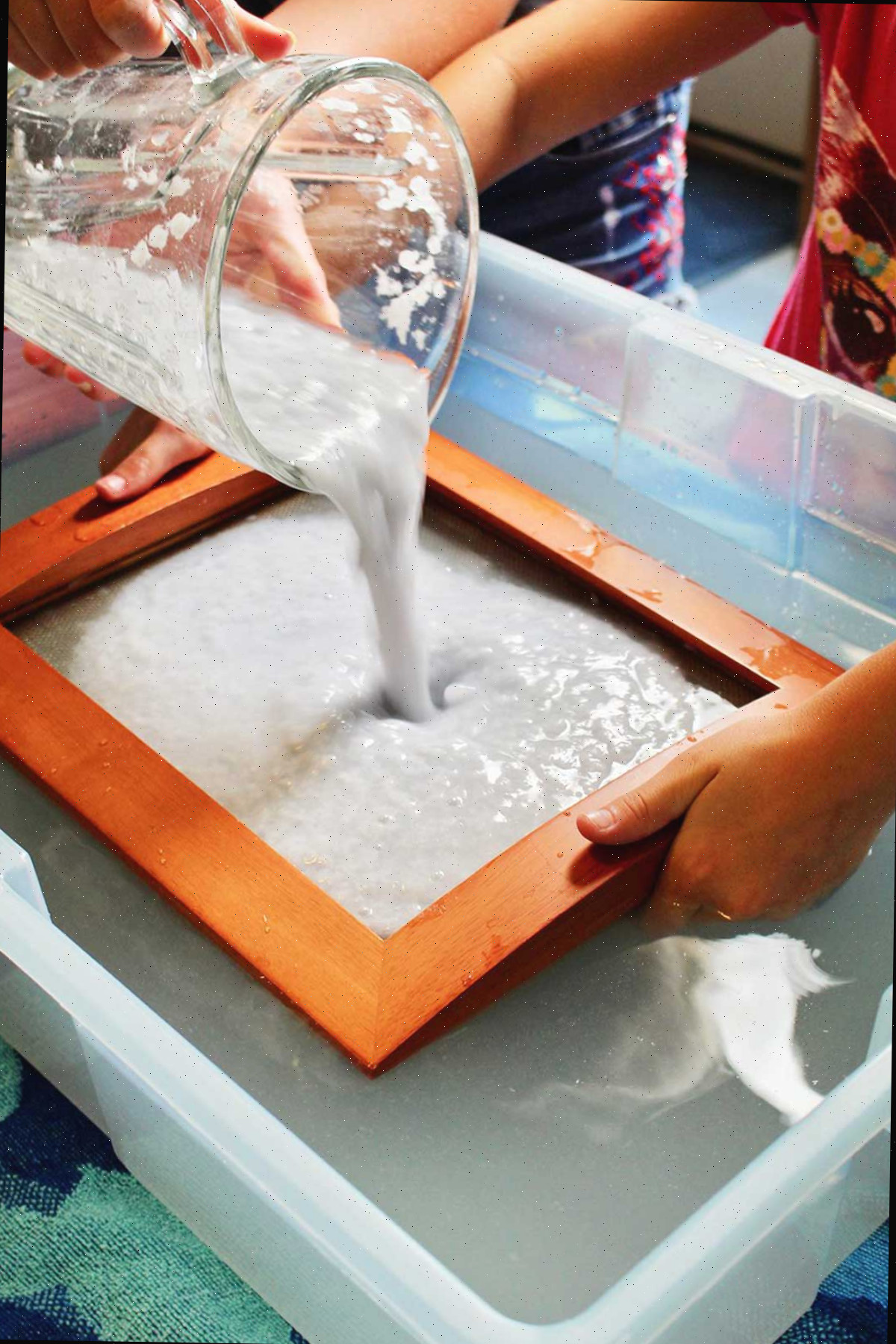 Despejando papel batido e água em um molde e moldura em uma caixa de água.