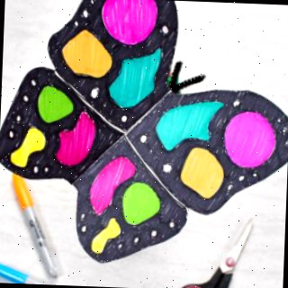 Artesanato de borboleta de papel completo colorido com marcadores preto e neon descansando perto de uma tesoura preta e marcadores neon.
