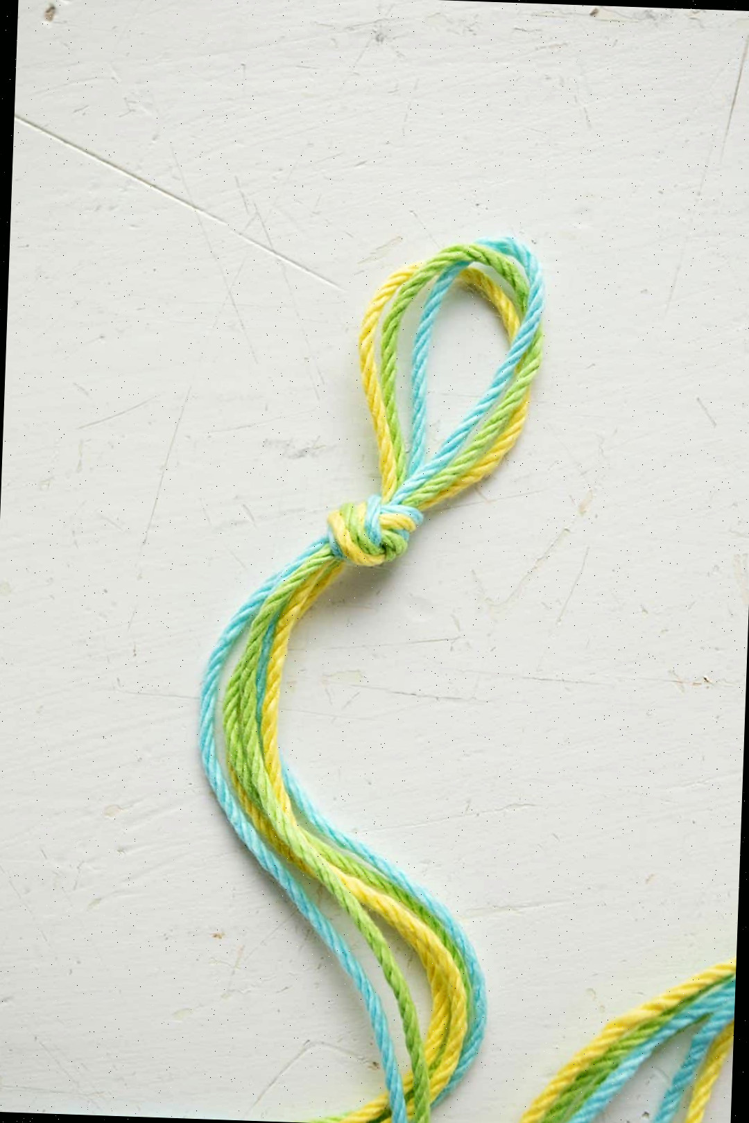 Uma pulseira em padrão Chevron sendo feita com cordão azul, verde e amarelo.