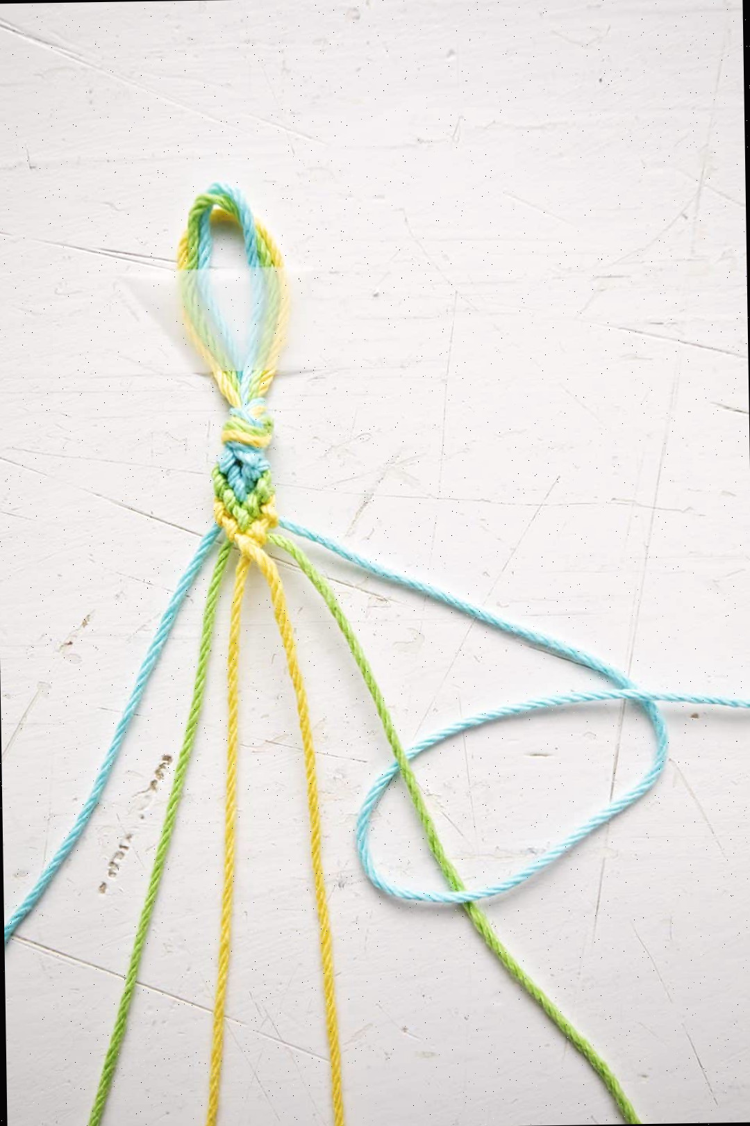 Uma pulseira com padrão Chevron sendo feita com fios azuis, verdes e amarelos.
