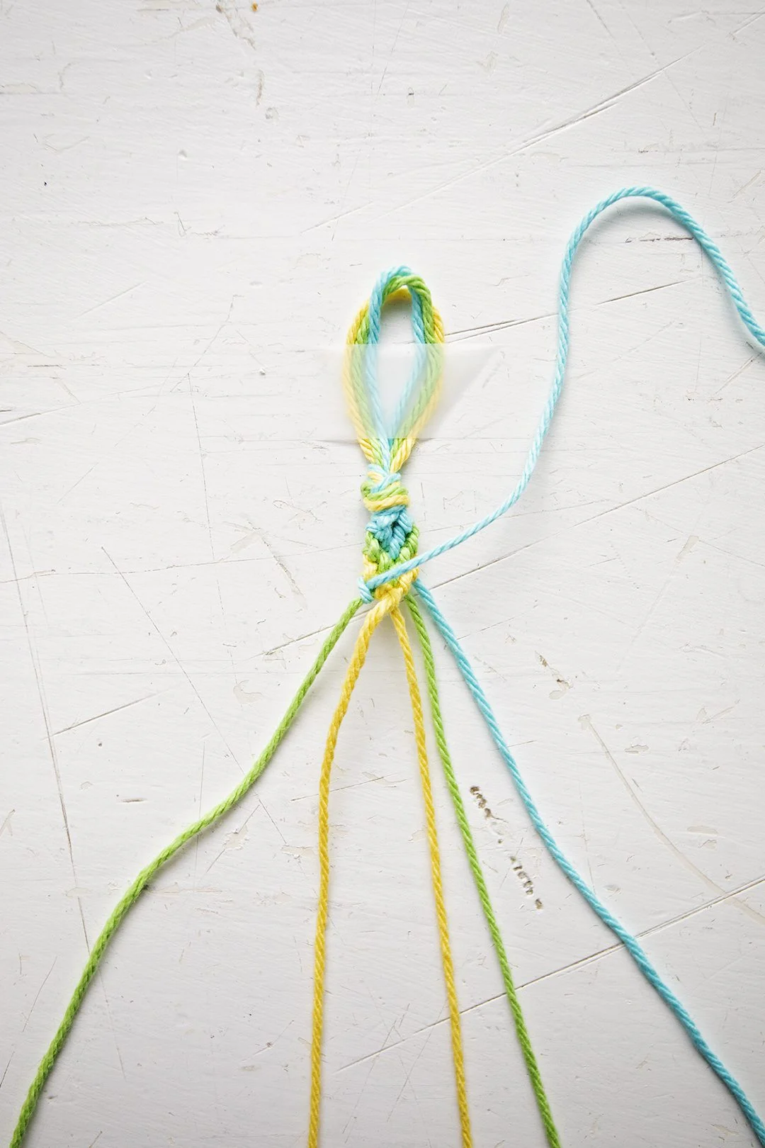 Um padrão de pulseira em Chevron sendo confeccionado a partir de fios azuis, verdes e amarelos.