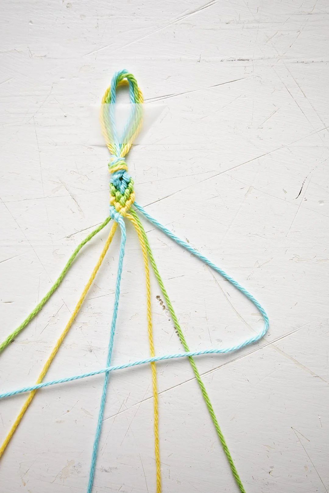 Um padrão de pulseira em Chevron sendo confeccionado a partir de fios azuis, verdes e amarelos.