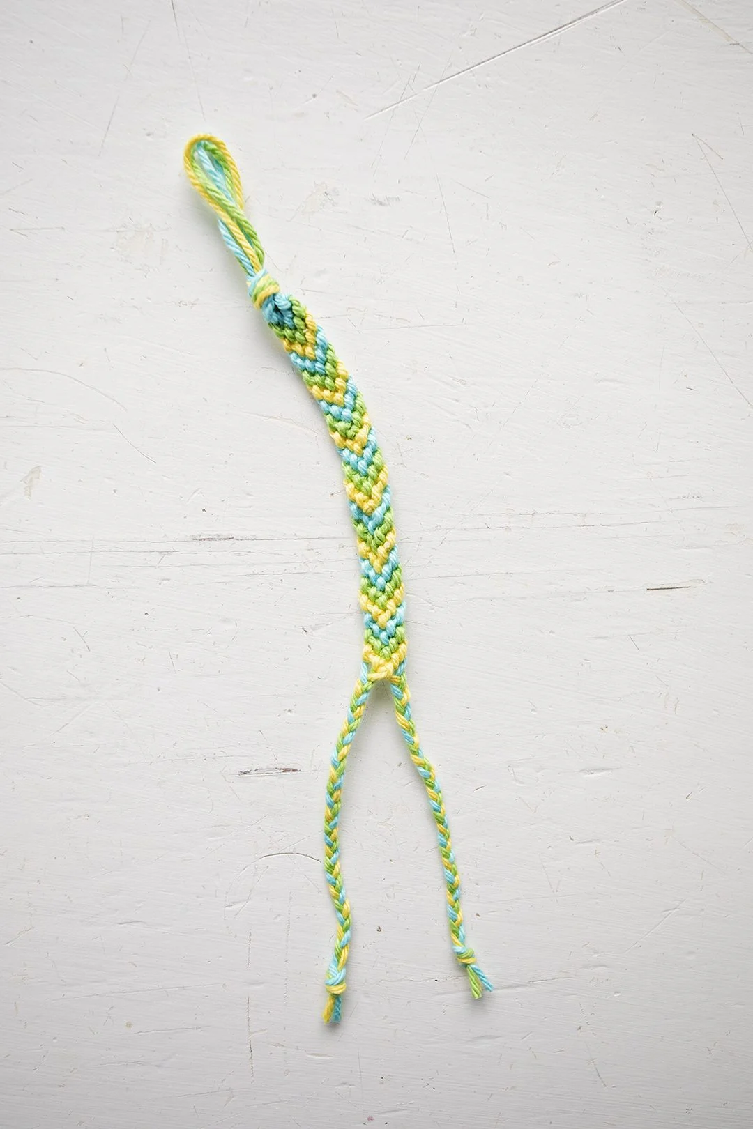 Um pulso de padrão chevron feito de cordões azuis, verdes e amarelos.