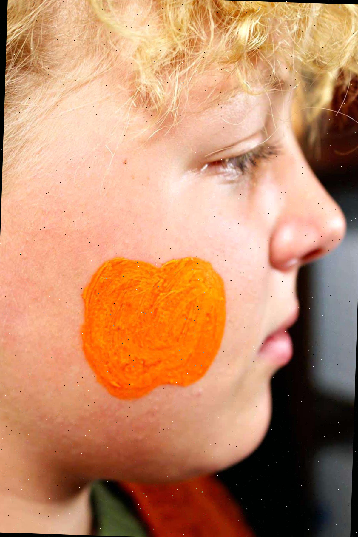 Perfil do rosto de uma menina com contorno de pintura facial laranja de uma abóbora na bochecha.
