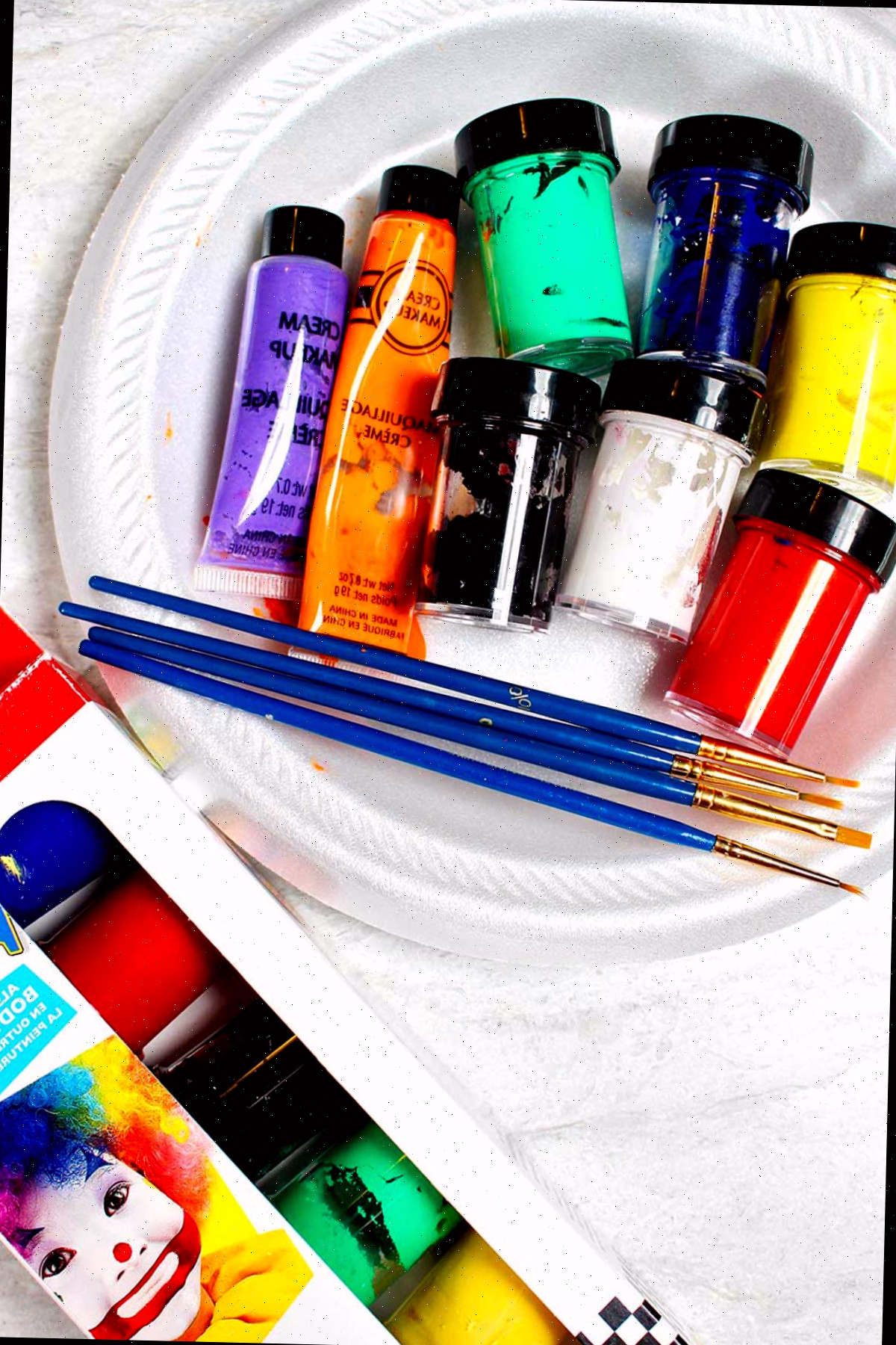 Prato branco com potes de tintas coloridas e pinceis de pintura ao redor.
