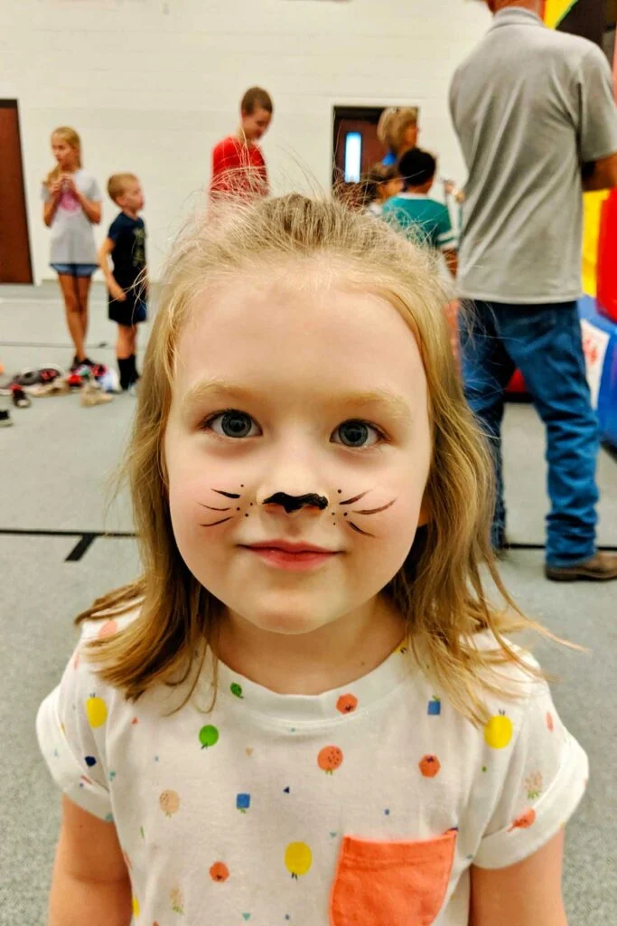 Menina jovem com pintura facial de gato preto.