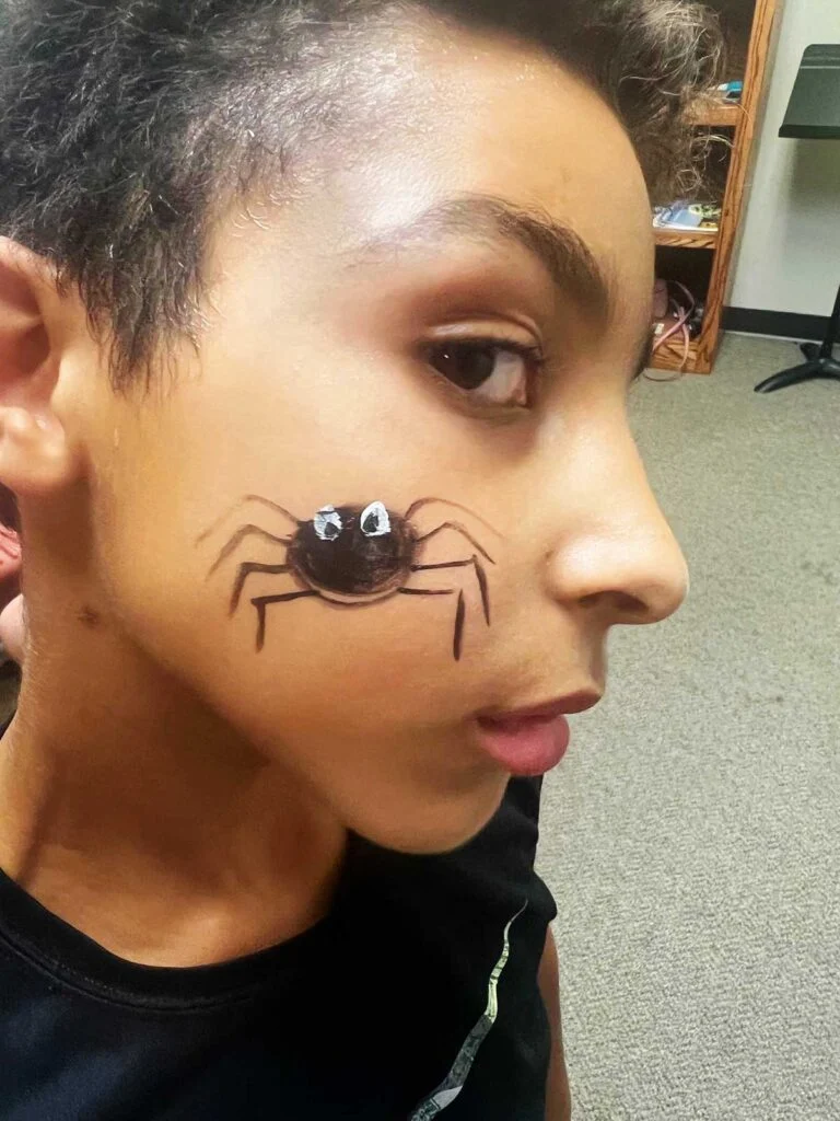 Menino jovem com uma camisa preta e pintura facial de aranha preta.