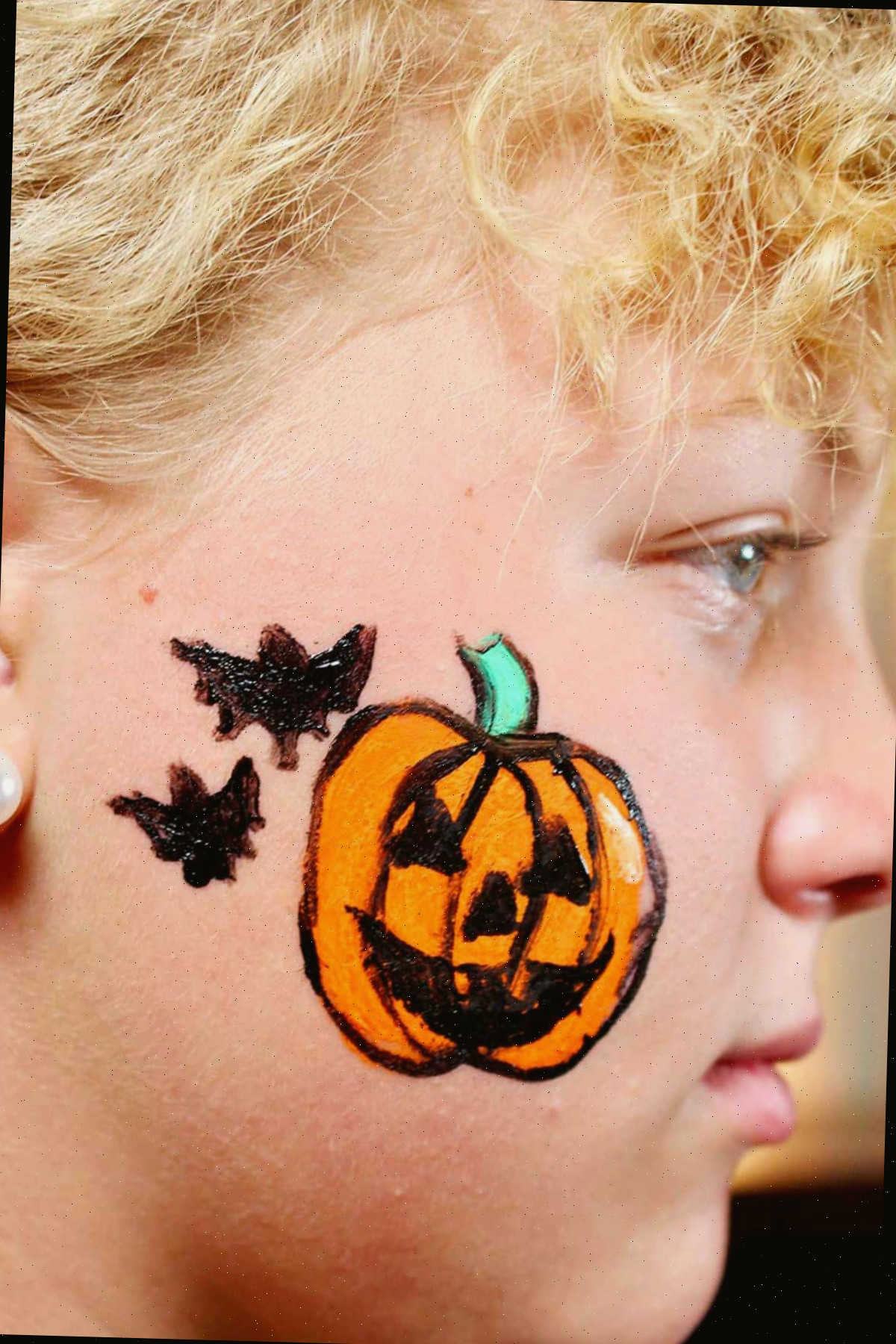 Perfil de uma menina com jack-o-lantern finalizado e dois morcegos pretos na bochecha.