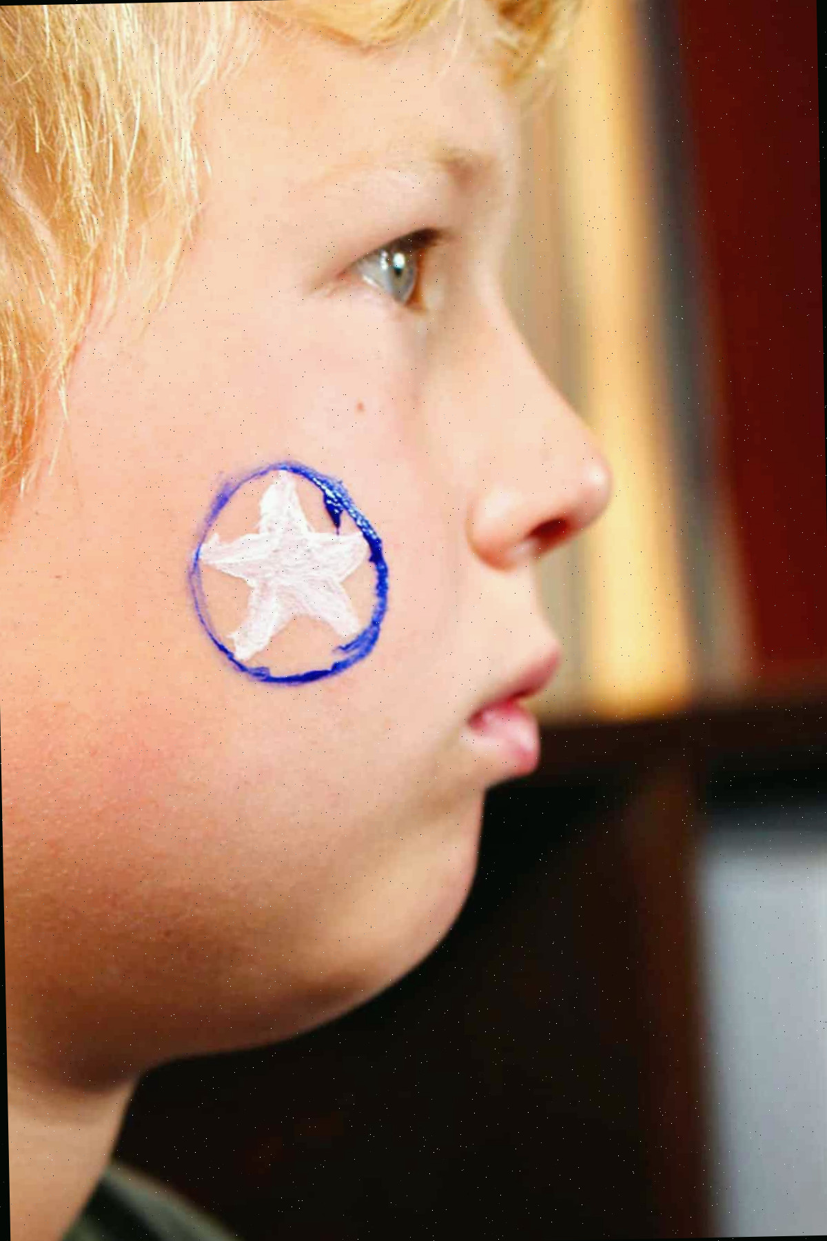 Perfil de menino com estrela branca e círculo azul ao redor pintado na bochecha.