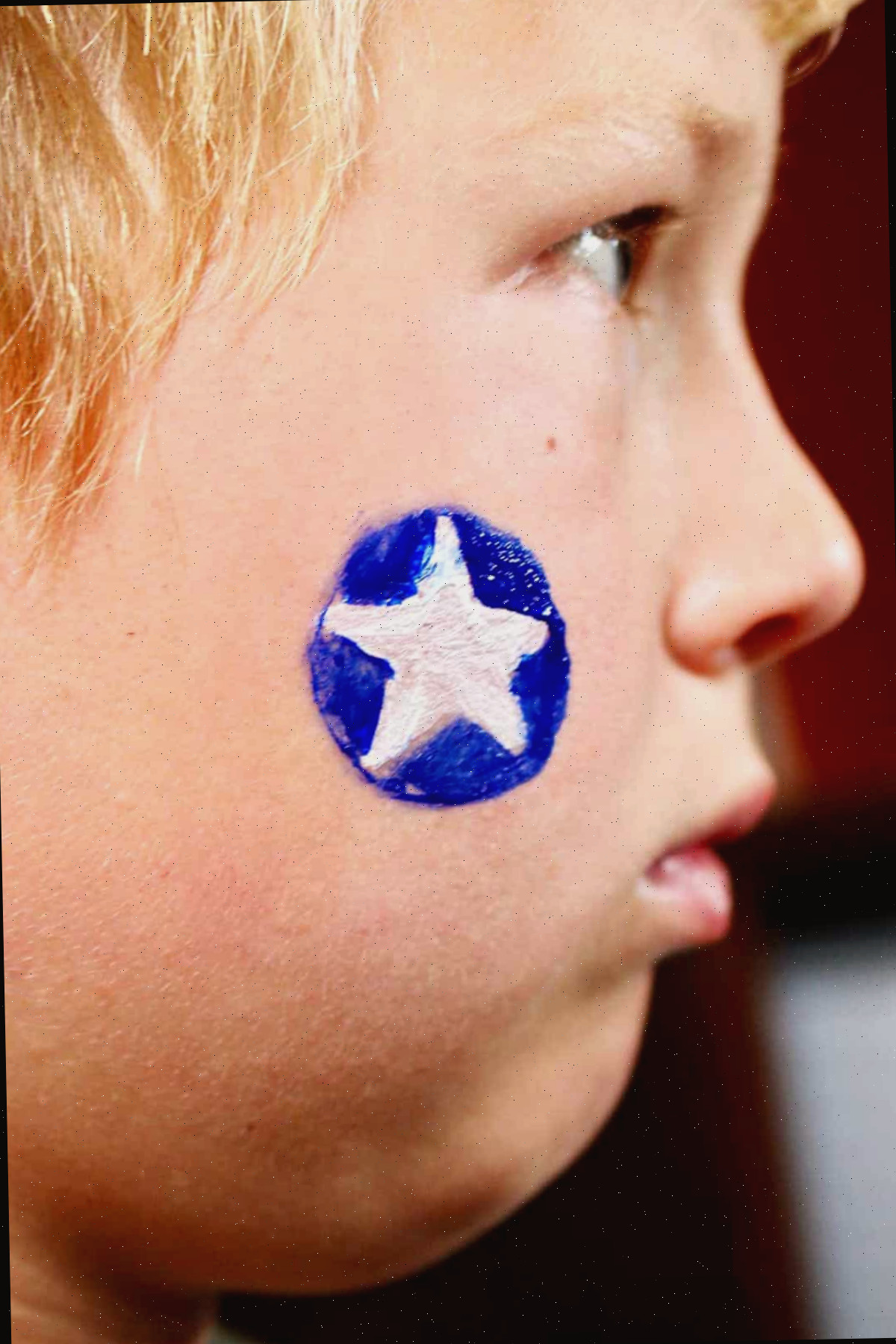 Perfil de menino com círculo azul e estrela branca pintada na bochecha.