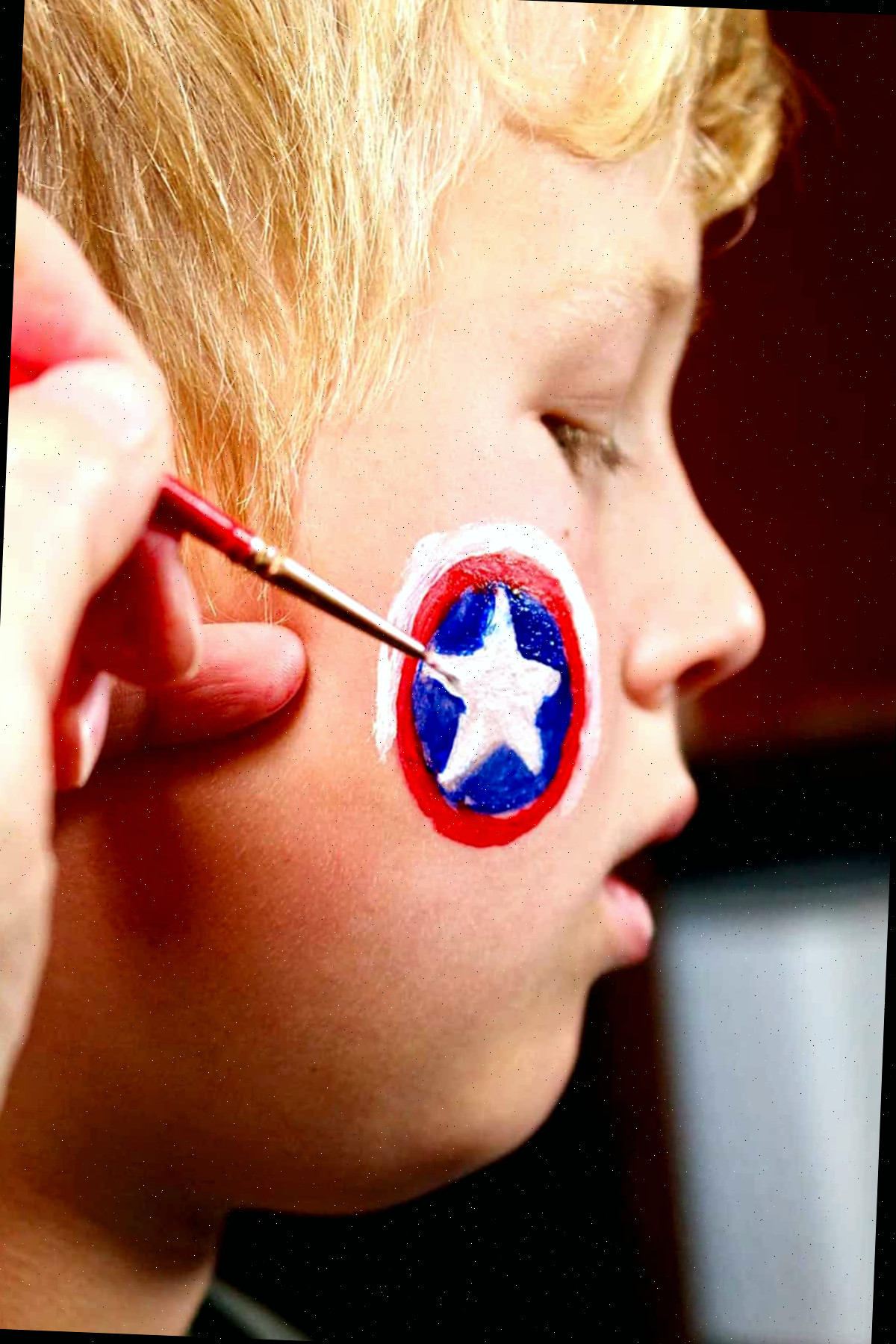 Perfil de menino com detalhes de pintura de mão do escudo do Capitão América na bochecha.
