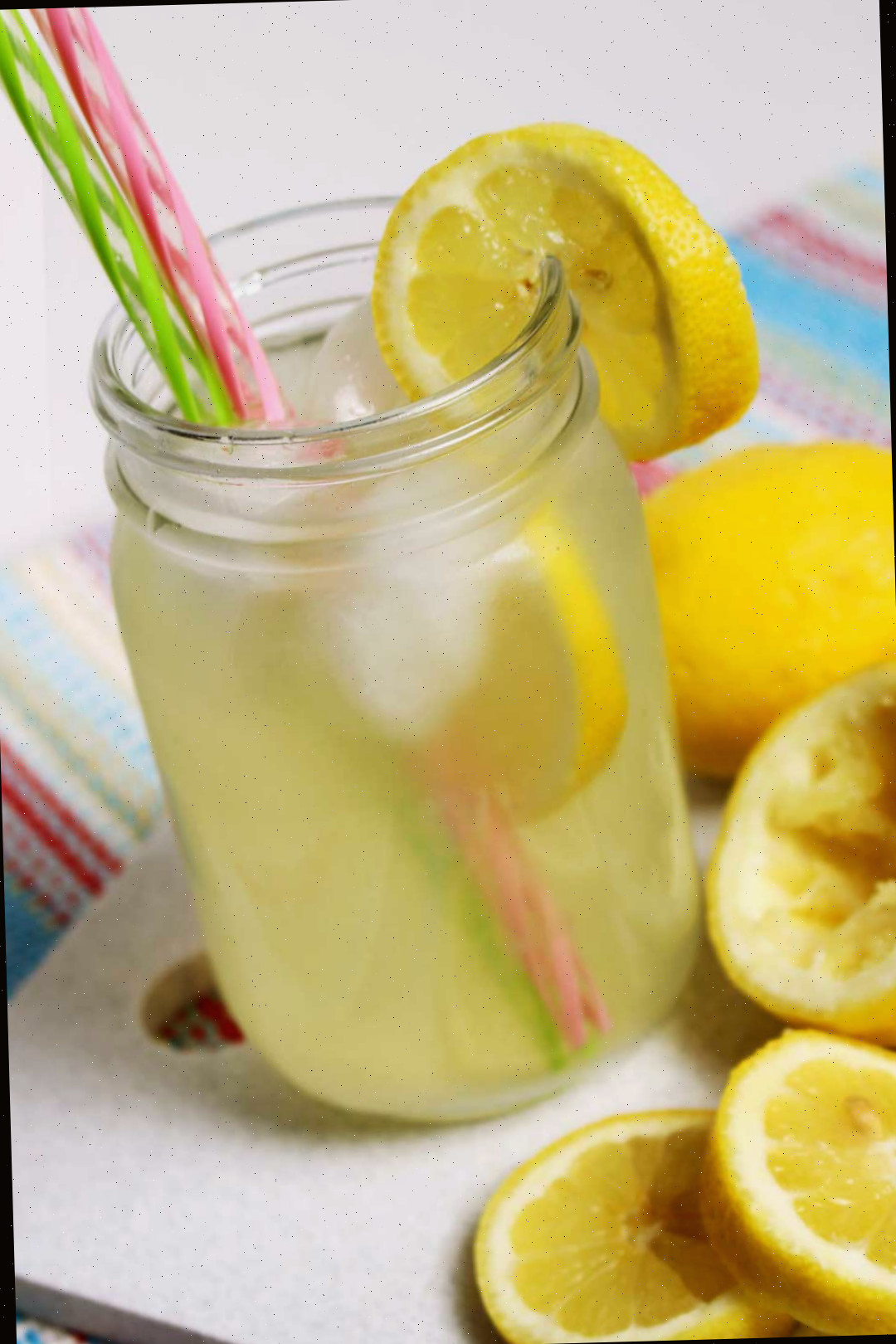 Um copo de limonada em um pote de conserva com canudos rosas e verdes próximo a algumas fatias de limão.