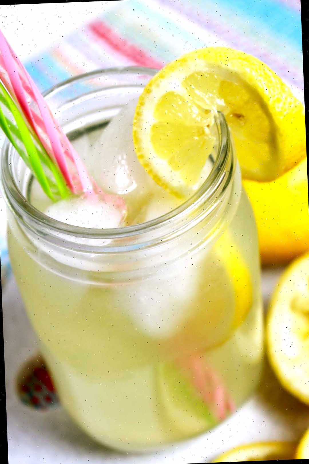 Um copo de limonada em um pote de conserva com canudos rosa e verde perto de algumas fatias de limão.