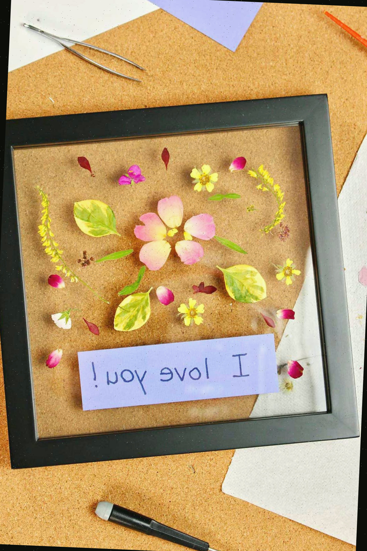Flores prensadas emolduradas com uma etiqueta roxa dizendo "Eu te amo!"