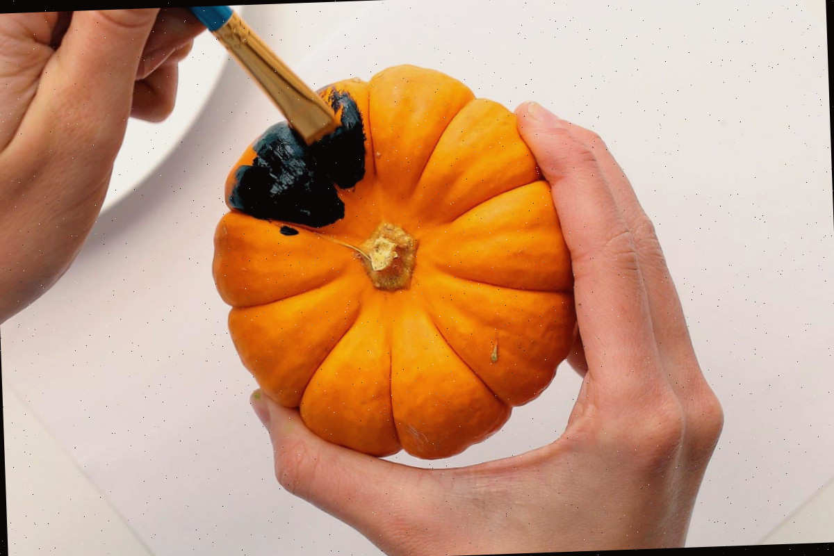 Um pincel pintando uma mini abóbora de preto.