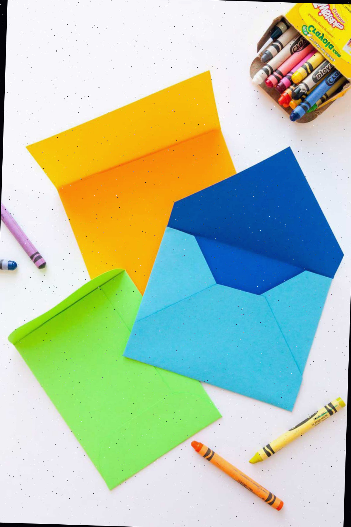 Um envelope artesanal azul, verde e laranja rodeado por giz de cera.