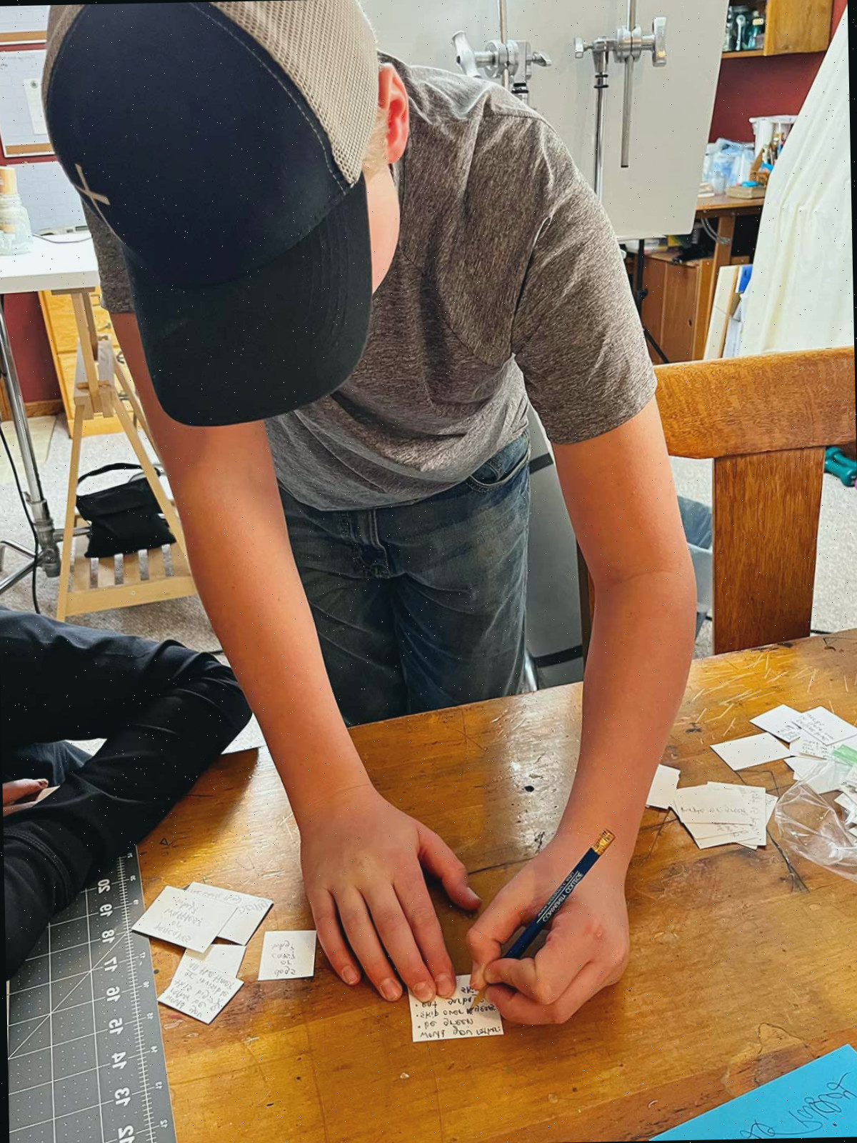 Um menino com um boné de beisebol escrevendo uma pergunta de 'Você Preferiria' em um pedaço de papel.