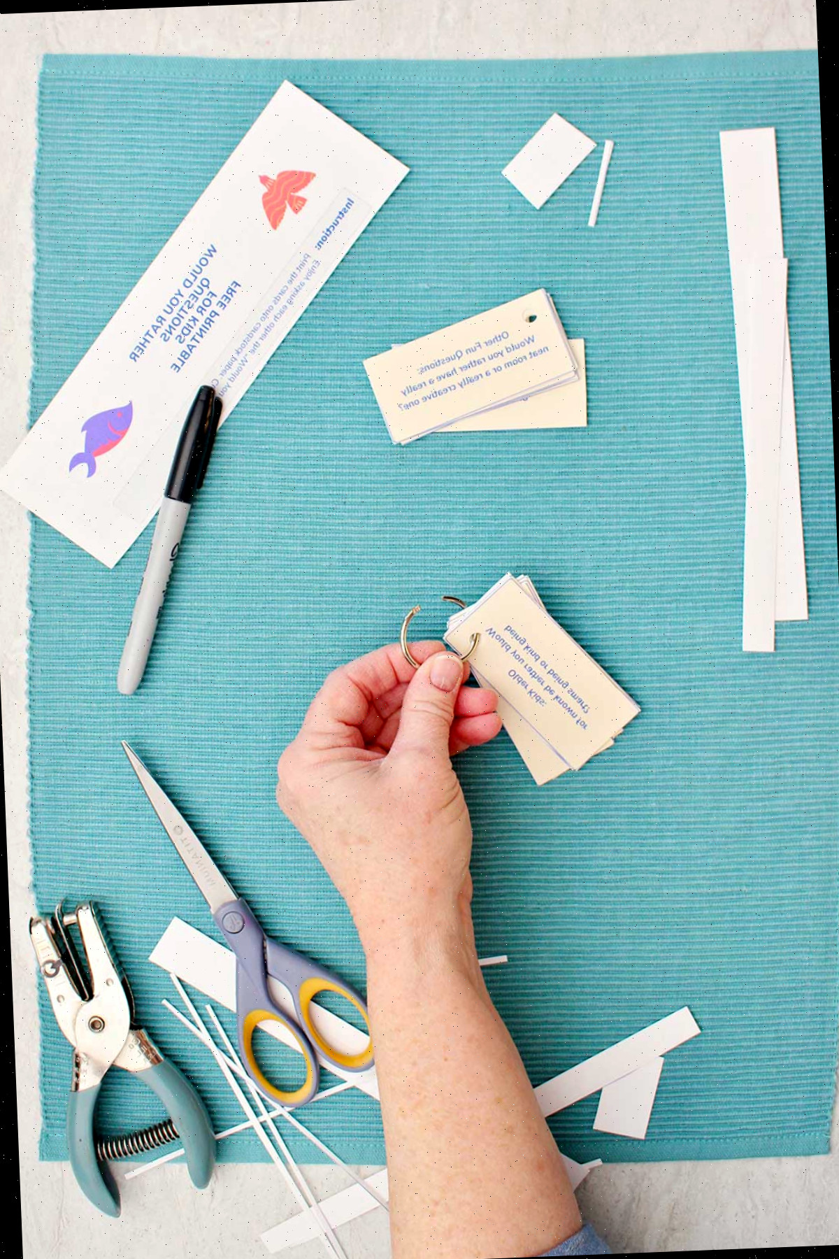 Alguém fechando o anel em uma pilha de questões Você Preferiria com pedaços de papel cortados, uma tesoura, um furador de papel e uma caneta próximos.