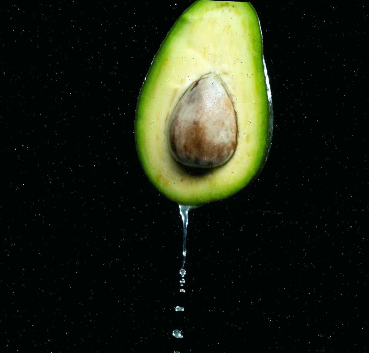 Use água para prevenir o escurecimento. Metade de abacate em um fundo preto com água gotejando abaixo dele.