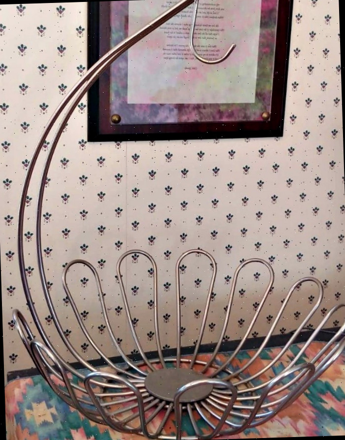 Suporte de metal para bananas sobre um caminho em teal e rosa na frente de uma imagem emoldurada com uma citação.