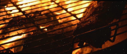 Brasas de churrasco sob uma grelha em chamas.