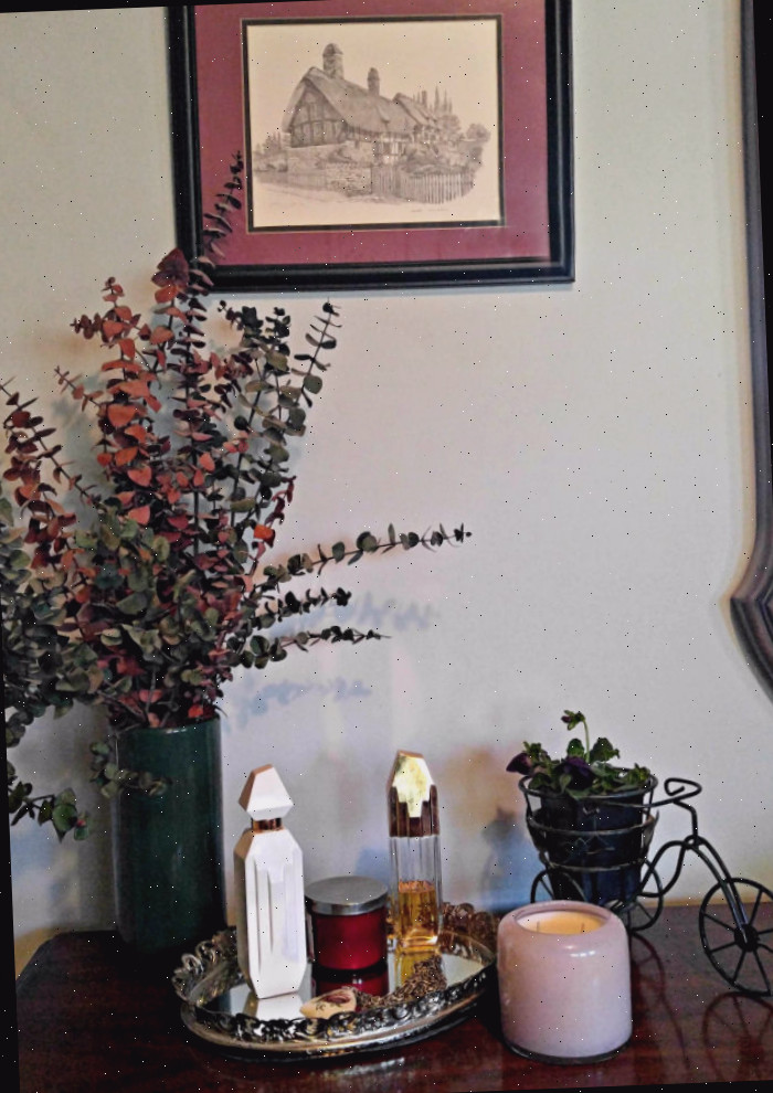 Uma exibição em uma cômoda de quarto com uma impressão de parede, flores secas, planta, bandeja com perfumes e uma vela em um suporte de vidro. Decoração instantânea para o quarto!