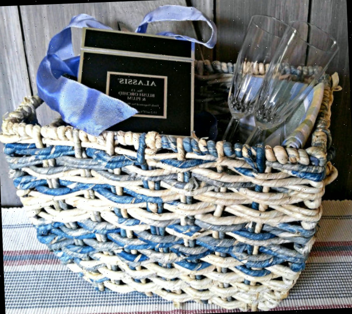 Uma cesta de presente azul repleta de guardanapos de mesa, duas taças de champanhe e uma vela em caixa com laço.