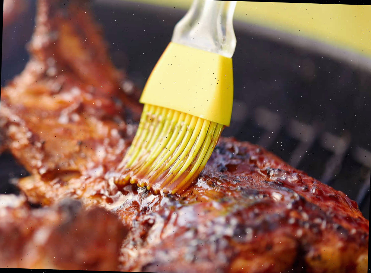 Adicionando molho barbecue Pincel de silicone amarelo adicionando molho barbecue à carne.