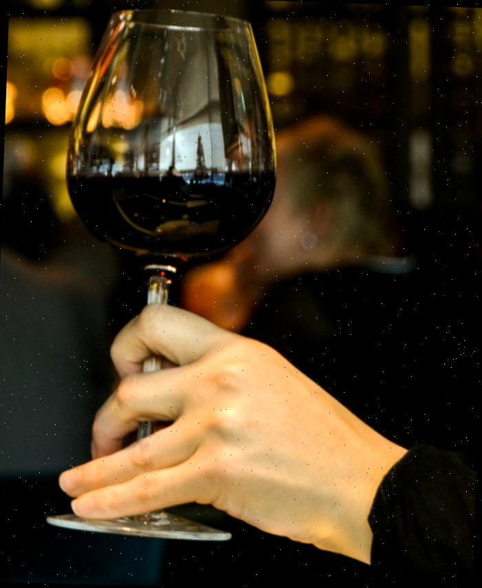 Mão feminina segurando um copo de vinho tinto.