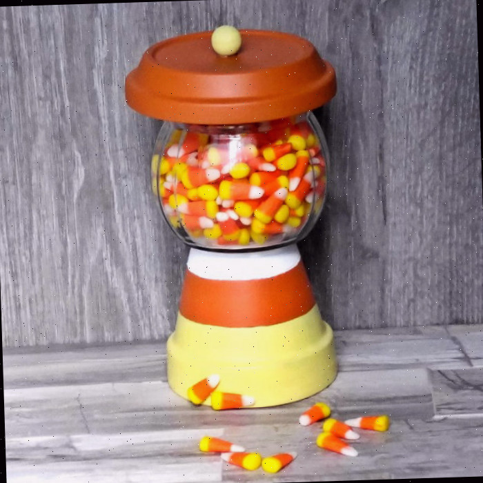 Um suporte DIY de doces de milho feito de vasos de barro, repleto de doces de milho em um balcão de madeira com alguns doces de milho ao lado.