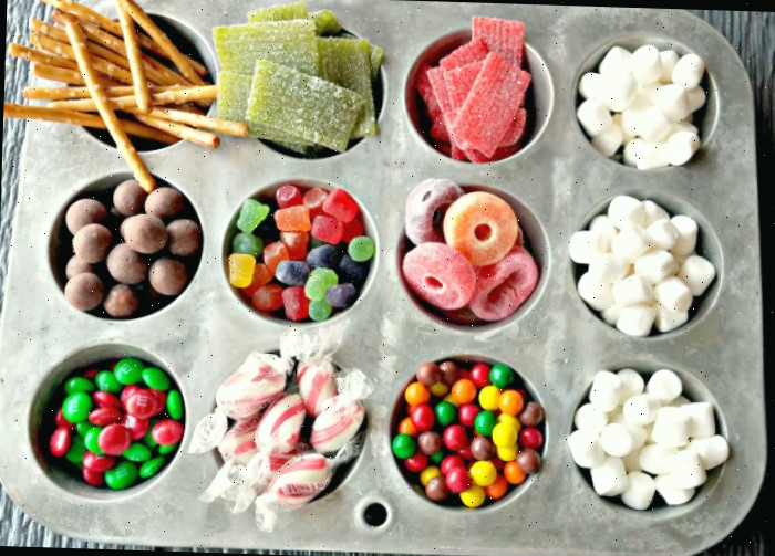 Marshmallows, bala listrada, bolinhas de leite maltado, Skittles, pretzels, gelatinas e M&Ms em uma forma de muffin, prontos para montar uma casa de gengibre.