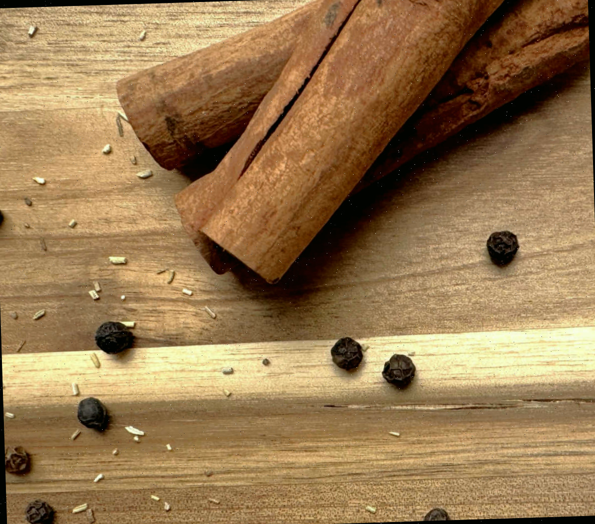 Paus de canela e grãos de pimenta-do-reino sobre uma bancada de madeira.