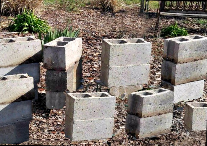 Blocos de concreto empilhados com um banco de jardim atrás deles Blocos de concreto empilhados prontos para serem feitos em uma cama elevada de jardim.