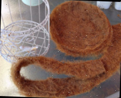 Uma gaiola branca sobre uma mesa com tesoura e algumas fibras de coco cortadas.