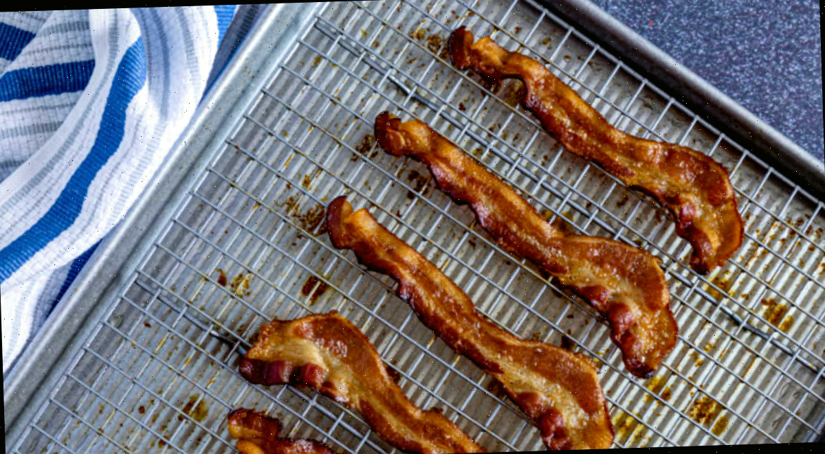Fatias de bacon crocante cozidas no forno sobre uma grade de arame e assadeira ao lado de uma toalha listrada azul.