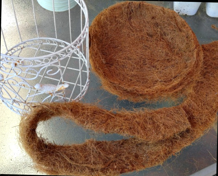 Um forro de fibra de coco cortado em uma mesa com algumas plantas pequenas e uma gaiola branca aberta.