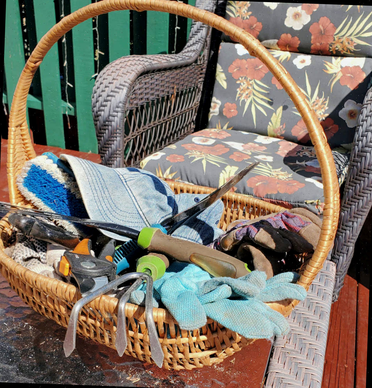 Uma cesta com ferramentas de jardinagem ao lado de uma cadeira de varanda.
