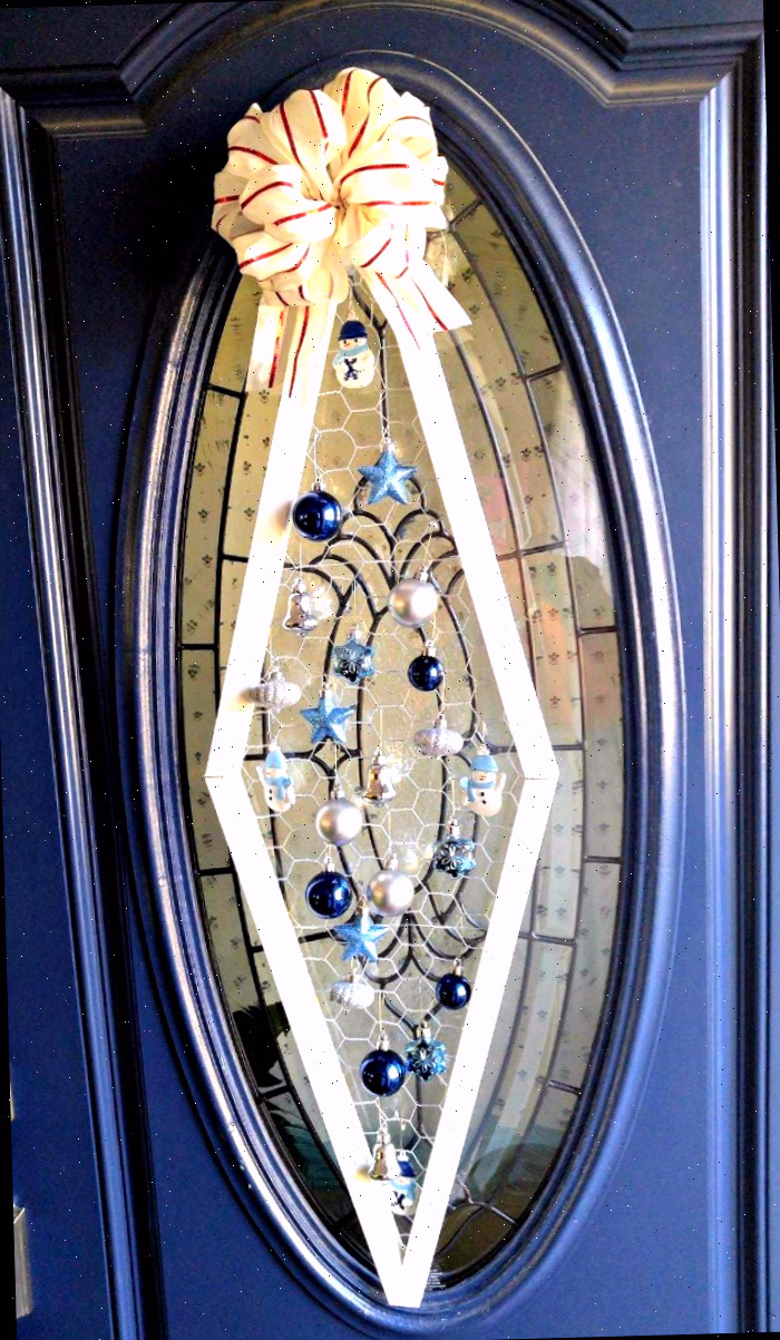 Decoração de porta com ornamento de Natal em uma porta azul com vidro oval.