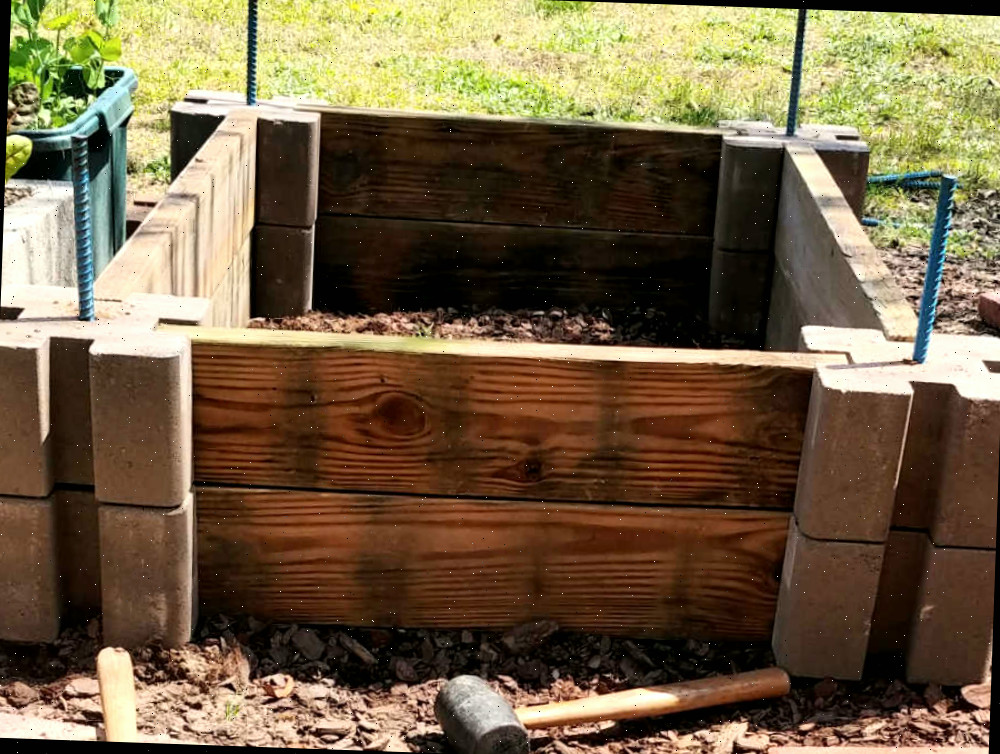 Martelando os suportes de rebar. Uma estrutura de cama de jardim feita de blocos de cimento e madeira com rebar para estabilização.