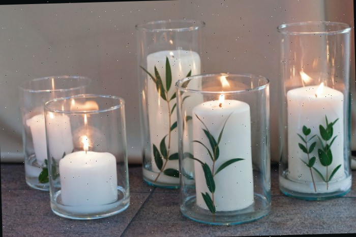 Velas brancas com folhas de eucalipto dentro dos suportes de velas.