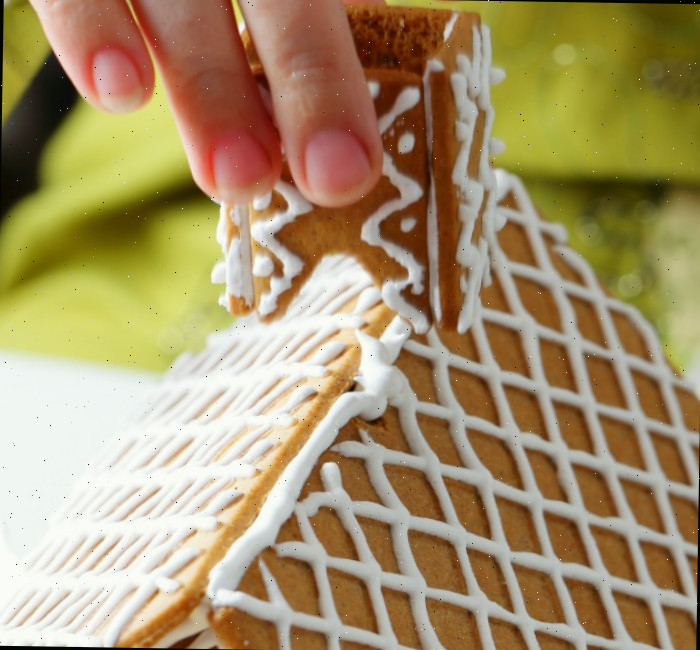 Mão segurando uma chaminé de gengibre acima do telhado decorado.