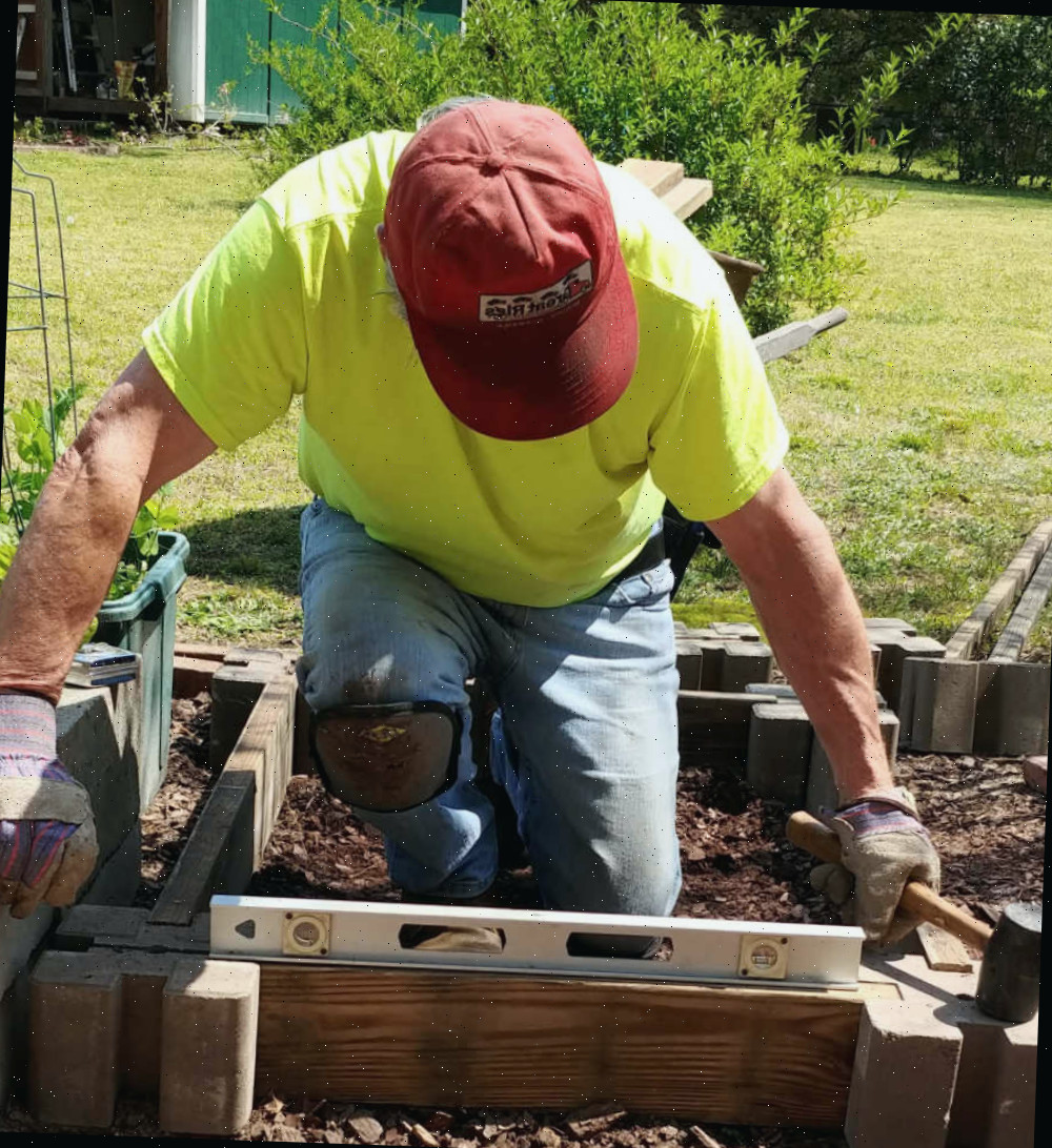 Nivelando os lados de uma cama de jardim. Homem utilizando um nível de bolha para garantir que os lados de uma cama de jardim elevada estejam retos.