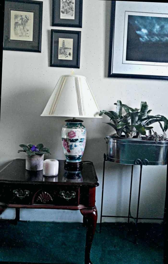 Uma única vela em uma mesa vazia com uma lâmpada e um vaso coordenados para adicionar clima à sua sala de estar.